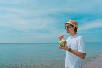 Tourist having a coconut drink on the beach. Young handsome man drinking coconut milk on the...