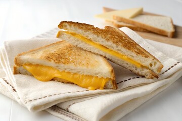A simple cheese sandwich cut diagonally, placed on a napkin, minimal white surface
