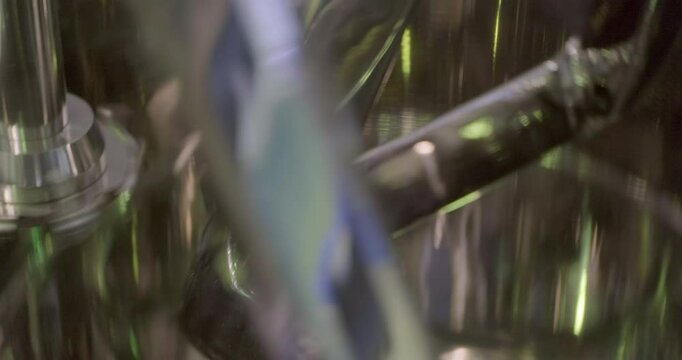 An industrial paint mixer is in operation, various attachments are moving and rotating inside the stainless steel bowl. Handheld close up shot, artificial lighting, real time speed.