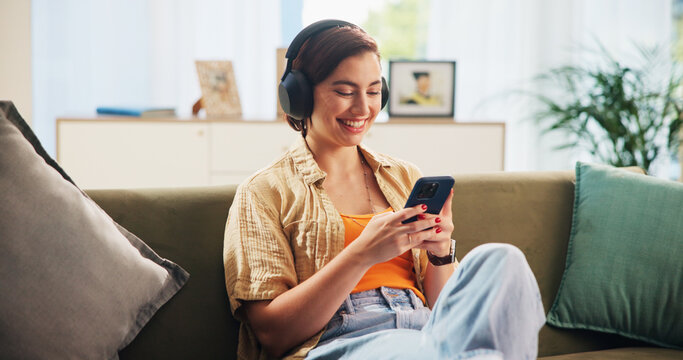 Woman, phone and headphones on sofa, happy and texting in home with streaming, audio and relax in lounge. Girl, smartphone and smile with mobile app for listening to music on couch at apartment