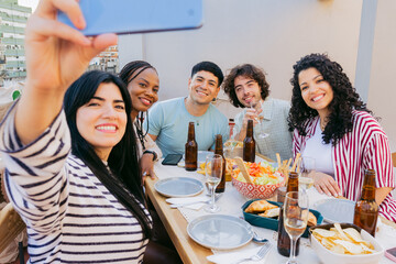 Young latina takes a selfie with friends, in front of a table with food, on a terrace at noon