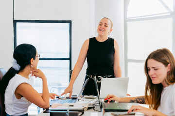 Fototapeta premium Young Latina entrepreneur, in an office with laptops, leading interactions with co-workers