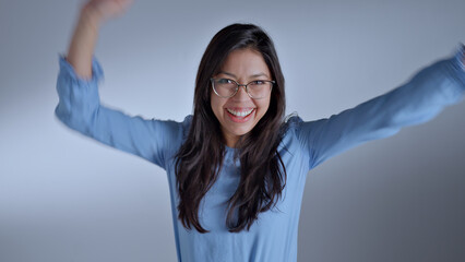 A woman in a blue shirt and glasses raises her arms, exuding joy and confidence. The close-up shot...