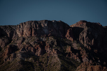 Photograph of dry rocky mountains with lights and shadows marked by sunset.