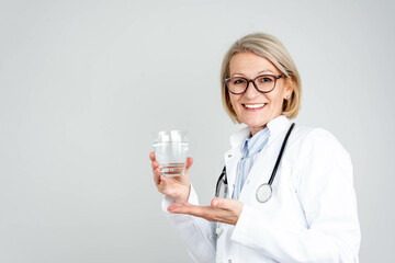 Smiling beautiful female doctor holding a glass of water in front of an isolated background....