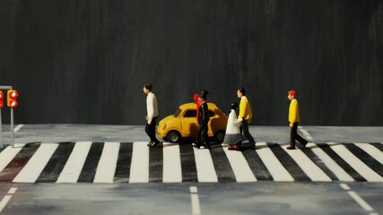 A group of people are crossing a street with a yellow car. The car is on the crosswalk and is being stopped by a person. The scene is a miniature model of a city street