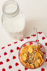 Tasty corn flakes with granola in bowl with bottle of milk. Rustic background with beautiful napkin with heart print. Healthy crispy breakfast snack. The concept of a healthy lifestyle.