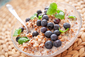 Buckwheat porridge with organic blueberries in a glass plate on a straw table mat. closeup