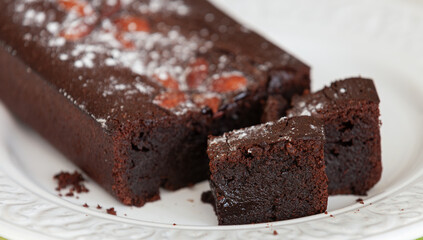 Closeup of juicy chocolate brownie of a pie decorated with sugar powder and almond on a glass plate.