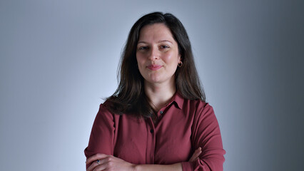 Fototapeta premium A woman in a red shirt stands confidently with a smile, exuding self-assurance and poise. The shot is a close-up, highlighting her expression and attire.