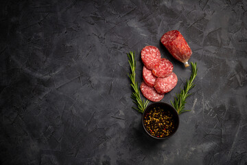 Salami with fresh rosemary and spices. on a black stone background. Top view. Free space for text.