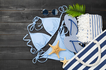 Blue bikini with beach accessories on wooden background, top view