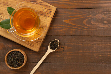 Cup of tea with dry and fresh leaves on wooden background, top view