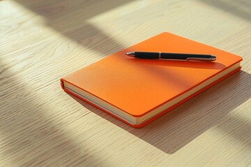 Orange Notebook and Pen on Wooden Desk Surface with Soft Shadows