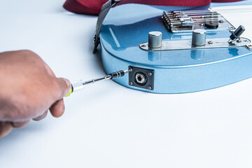 Close-up of a hand using a screwdriver to repair or install the input jack on an electric guitar....