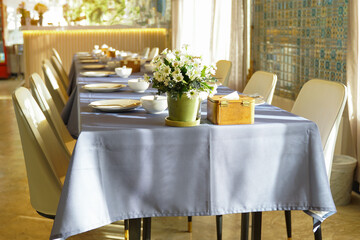 The dining table is covered with a gray tablecloth, looking elegant. On the table, a set of tableware is arranged neatly and ready for use, and decorated with a vase of flowers.