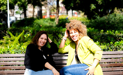 Two smiling businesswomen relaxing on park bench during work break