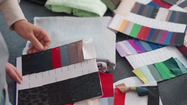 Fashion designers selecting fabric colors from vibrant color panels at creative workspace filled with colorful textile samples, folded fabrics, and pattern sheets for inspiring fashion projects