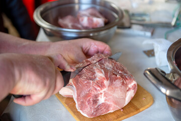 Person slicing raw pork meat on cutting board with stainless steel bowls around.