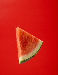 A single slice of juicy watermelon is centered against a bold red background