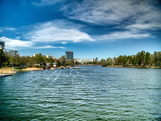 Fototapeta premium Spring Breeze on the Old Danube A vivid spring day on the Old Danube in Vienna. Calm waters, lush greenery, and modern skyline blend urban life with nature in this peaceful view of Kaisermühlen.