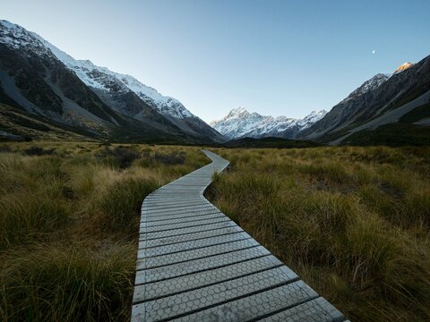 Wooden walkway boardwalk hiking trail path leading to alpine snow covered Southern Alps mountains, Hooker Valley Track, Aoraki Mount Cook New Zealand