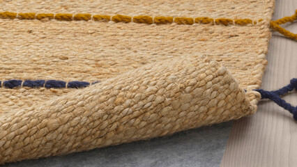 Textured woven rug displayed indoors with rolled edge and colorful accents on a wooden floor.