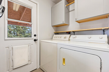 A laundry room that features numerous cabinets, a sink, and a window