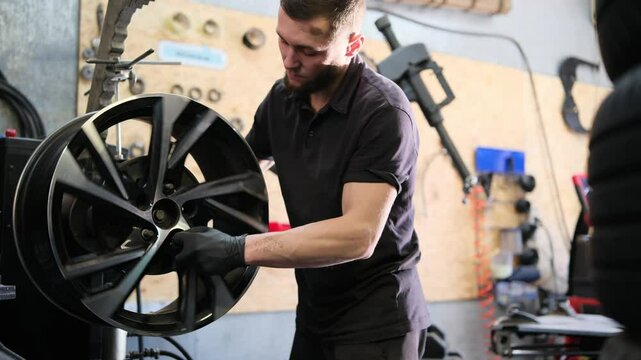 A mechanic secures a car rim to a device to repair it