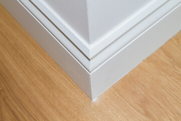 Corner of a white baseboard on a parquet floor