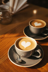 two latte cups with heart-shaped latte on wooden table