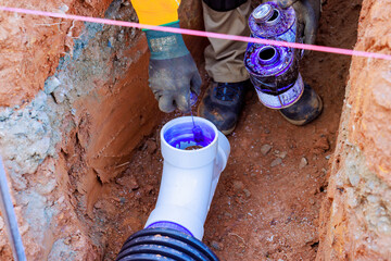 Plumber worker is gluing pvc pipe in trench to conduct plumbing repairs hands on labor.