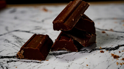 Stack of broken chocolate pieces on marble surface with cocoa shavings
