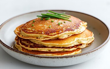 Delicious golden pancakes stacked on a plate, garnished with fresh chives. A simple, appetizing food photograph