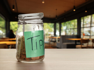 Tips jar with money on light wooden table in cafe, space for text