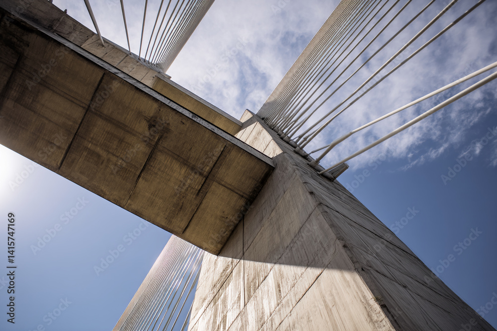Poster low-angle view of a bridge's concrete structure and cables against a blue sky, showcasing architectu