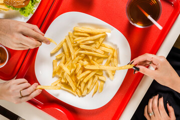 hands picking up french fries at fast food restaurant table, top view.