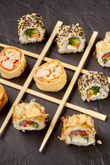 Variety of sushi rolls forming a tic-tac-toe game with chopsticks on dark background