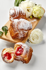 Delicious puff pastry cruffins with strawberry filling and icing sugar on wooden board