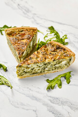 Delicious spinach and feta quiche slices with fresh arugula on marble