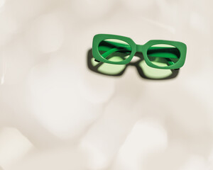 Fototapeta premium Top view Stylish green colored sunglasses with transparent green glass on beige background, shadow and glare at sunlight, summer fashion plastic-framed eyeglasses. Summer concept, copy space