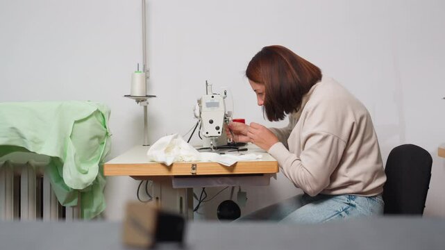 Dress maker performs machine maintenance by clipping stuck thread with precise care, ensuring smooth sewing in organized workspace, highlighting calm posture throughout the process