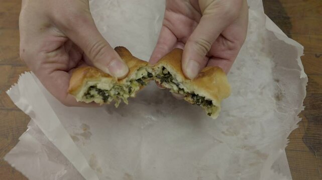 This video shows a close up view of hands tearing a spinach and cheese middle eastern bakery pie in half.