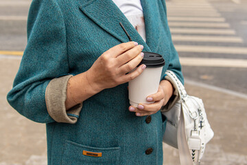 Woman holds coffee paper cup on street. Coffee to go. Natural