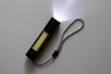 Small pocket portable black flashlight with led lights shine on white in the dark