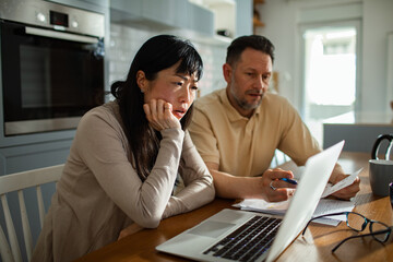 Concerned couple doing financials with laptop in modern home kitchen