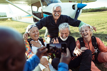 Group of happy senior skydivers posing for photo after landing near airplane