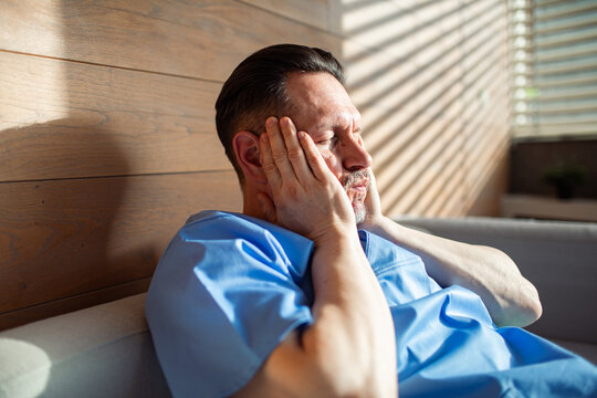 Tired male nurse sitting on couch with hands on face after long shift