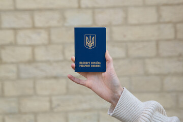 A person holds a Ukrainian passport with a blue cover displaying the national emblem against a...