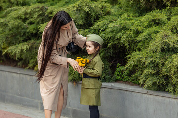 Patriotic education of children. Mother with little girl on Victory Day. Girl in a military uniform, military cap, holds flowers in hands near the memorial. Photo for the May 9 celebrations